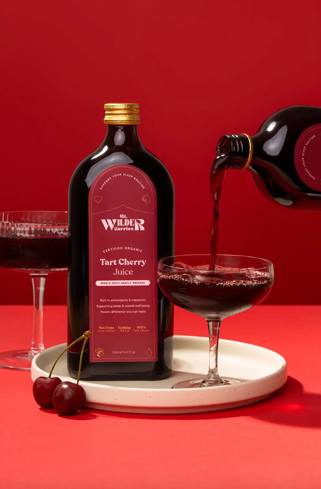 Wilder Tart Cherry Juice being poured into a glass with a red background