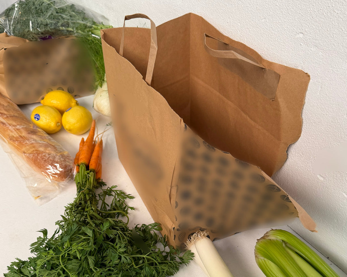 Brown paper bag with groceries including lemons, carrots, and celery on a white surface.